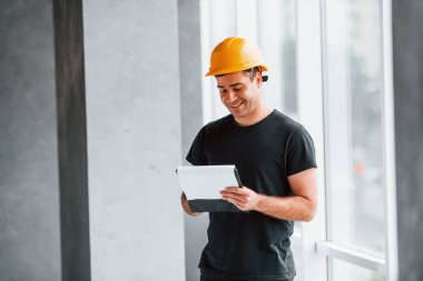 Sarı şapkalı erkek işçi ya da mühendis elinde not defteriyle evin içinde dikiliyor..