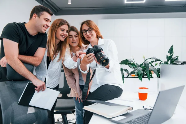 Ofiste resmi giyinmiş bir grup iş adamı kameradaki fotoğraflara bakıyor..