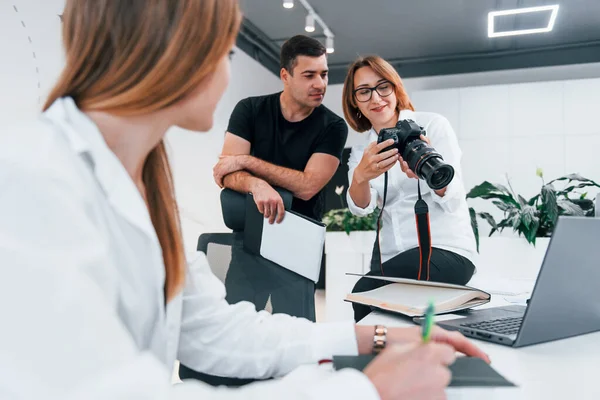 Ofiste resmi giyinmiş bir grup iş adamı kameradaki fotoğraflara bakıyor..