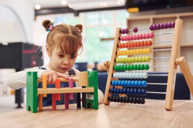 Anaokulunda oyuncaklarla oynayan günlük giysiler içinde neşeli küçük bir kız..