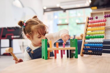 Anaokulunda oyuncaklarla oynayan günlük giysiler içinde neşeli küçük bir kız..
