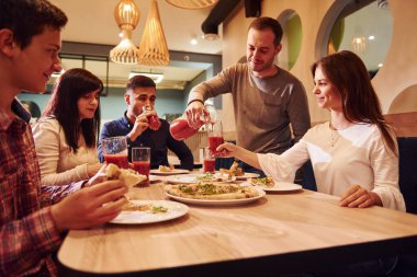 Evde oturup pizza yiyen bir grup genç arkadaş..