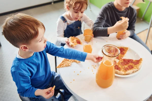 Three Children Sitting Indoors Table Eating Pizza Orange Juice Together — Stock Photo, Image