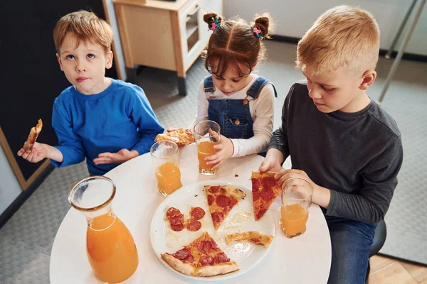 Three Children Sitting Indoors Table Eating Pizza Orange Juice Together — Stock Photo, Image