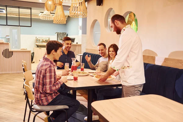 Chef delivers food. Group of young friends that sitting together indoors and eating pizza.