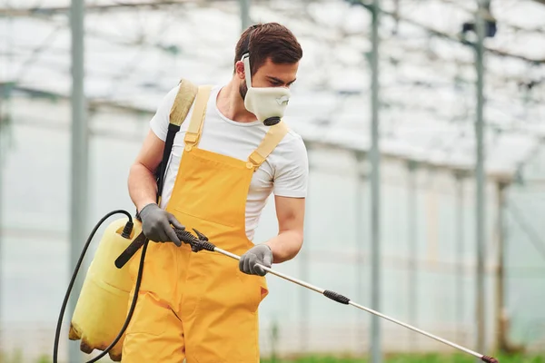 Young Greenhouse Worker Yellow Uniform White Protective Mask Watering Plants — Foto Stock
