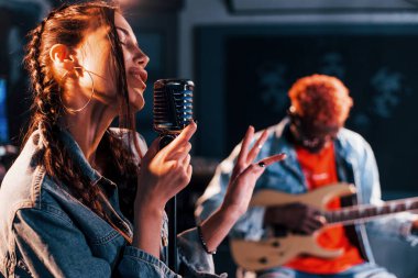 Guy plays guitar, girl sings. African american man with white girl rehearsing in the studio together.