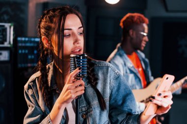 Guy plays guitar, girl sings. African american man with white girl rehearsing in the studio together.