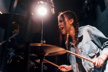 Plays drums. Young beautiful female performer rehearsing in a recording studio.