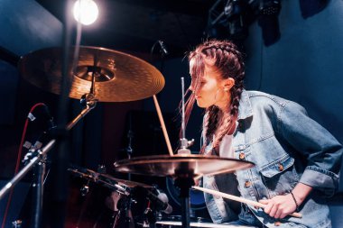 Plays drums. Young beautiful female performer rehearsing in a recording studio.