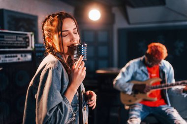 Guy plays guitar, girl sings. African american man with white girl rehearsing in the studio together.