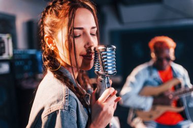 Guy plays guitar, girl sings. African american man with white girl rehearsing in the studio together.