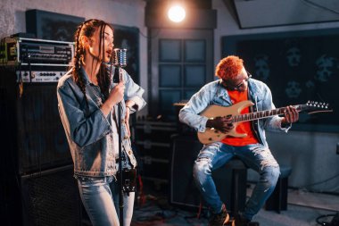 Guy plays guitar, girl sings. African american man with white girl rehearsing in the studio together.