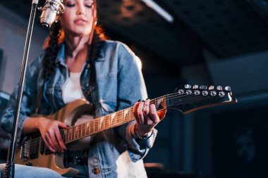 Gitar çalan ve bir kayıt stüdyosunda prova yapan genç ve güzel bir bayan sanatçı..