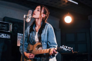 Gitar çalan ve bir kayıt stüdyosunda prova yapan genç ve güzel bir bayan sanatçı..