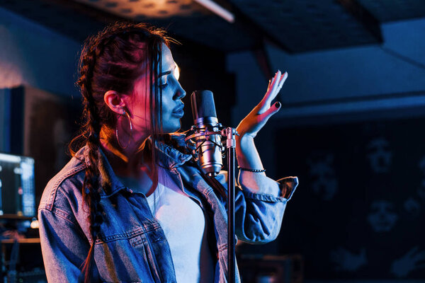 Young beautiful female performer sings and rehearsing in a recording studio.