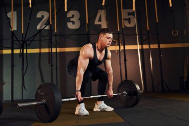 Spor elbiseli güçlü bir adam spor salonunda halter kaldırıyor..