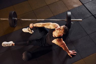 Spor elbiseli, yerde oturup spor salonunda mola veren güçlü bir adam manzarası..