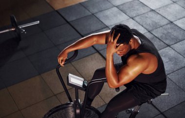 Bisiklete binmek. Spor elbiseli güçlü Afrikalı Amerikalı adam spor salonunda antrenman yapıyor..