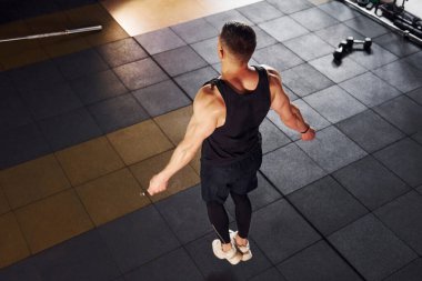 Spor elbiseli güçlü bir adam atlama ipi kullanarak spor salonunda antrenman yapar..