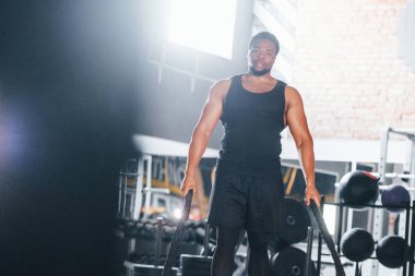 Güçlü Afro-Amerikan spor elbiseli adam spor salonunda antrenman yapıyor. Halat kullanarak Crossfit yapıyor.