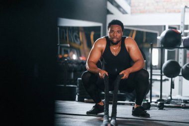 Güçlü Afro-Amerikan spor elbiseli adam spor salonunda antrenman yapıyor. Halat kullanarak Crossfit yapıyor.