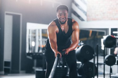Güçlü Afro-Amerikan spor elbiseli adam spor salonunda antrenman yapıyor. Halat kullanarak Crossfit yapıyor.