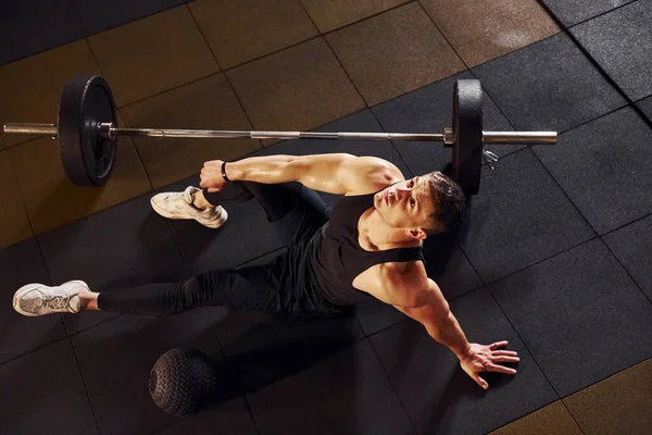 Spor elbiseli, yerde oturup spor salonunda mola veren güçlü bir adam manzarası..