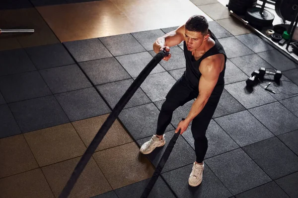 Spor elbiseli güçlü bir adam spor salonunda halat kullanarak antrenman yapar..