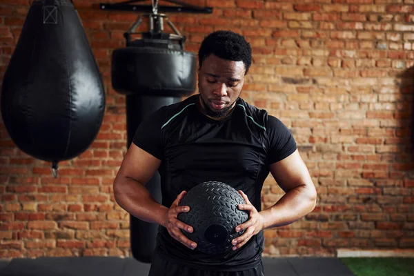 Spor salonunda spor elbiseli ve elinde topla güçlü bir Afro-Amerikan erkeği..