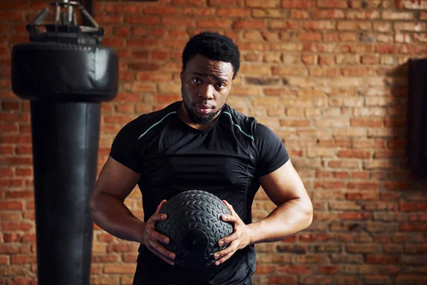 Spor salonunda spor elbiseli ve elinde topla güçlü bir Afro-Amerikan erkeği..