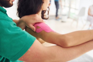 Adam fizyoterapi bandı takıyor. Formda vücut tipi olan genç bir kadın rehabilitasyon kliniğine gidiyor. Eğitmen ona yardım ediyor..