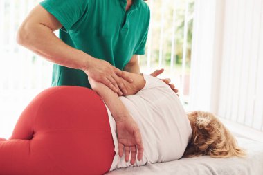 Yaşlı kadın kliniği ziyaret ediyor, uzanıyor ve rehabilitasyon görüyor. Erkek eğitmen ona yardım ediyor..