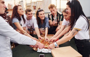 Lezzetli pizzayla. Gündelik giysiler içinde bir grup genç gündüz vakti çatıda parti veriyor..