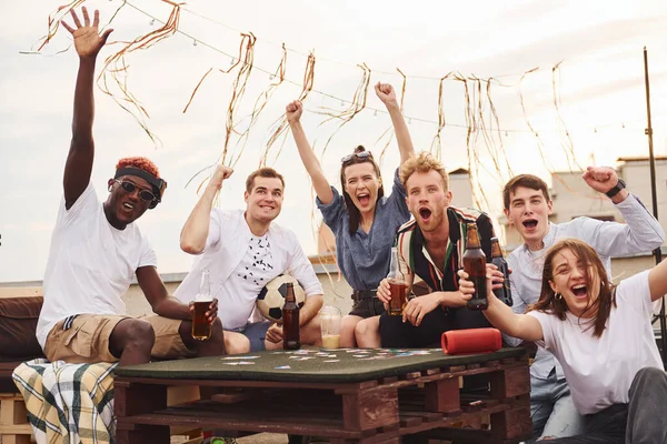 Kağıt oynuyorum. Gündelik giysiler içinde bir grup genç gündüz vakti çatıda parti veriyor..