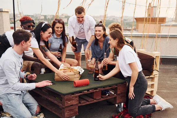 Lezzetli pizzayla. Gündelik giysiler içinde bir grup genç gündüz vakti çatıda parti veriyor..