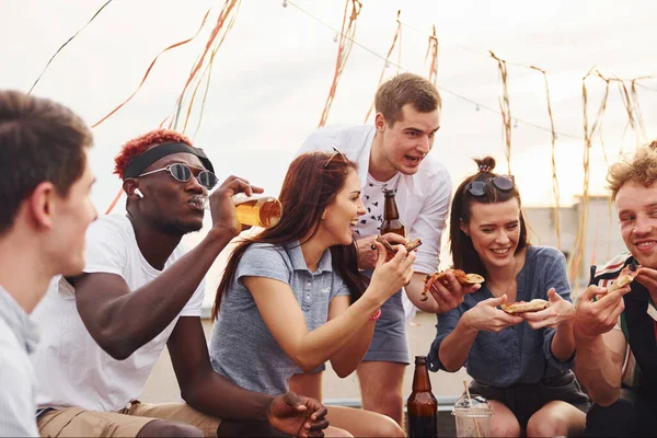Lezzetli pizzayla. Gündelik giysiler içinde bir grup genç gündüz vakti çatıda parti veriyor..