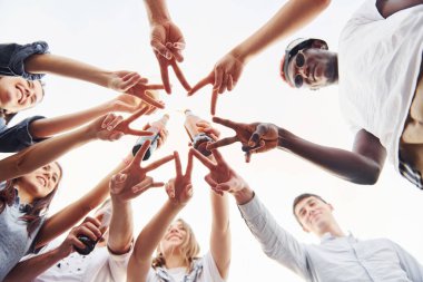 Parmaklarıyla güzel bir jest yapıyor. Aşağıdan bak. Gündelik giysiler içinde bir grup genç gündüz vakti çatıda parti veriyor..