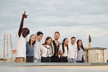 Süslü bir yer. Hava bulutlu. Gündelik giysiler içinde bir grup genç gündüz vakti çatıda parti veriyor..