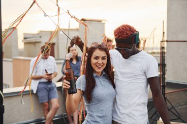 Kamera için poz vermek. Gündelik giysiler içinde bir grup genç gündüz vakti çatıda parti veriyor..