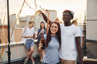 Kamera için poz vermek. Gündelik giysiler içinde bir grup genç gündüz vakti çatıda parti veriyor..