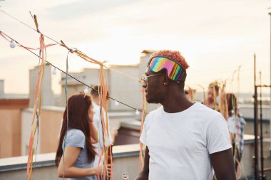 Kamera için poz vermek. Gündelik giysiler içinde bir grup genç gündüz vakti çatıda parti veriyor..