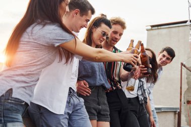 Çatının kenarına süslemelerle yaslanarak. Gündelik giysiler içinde bir grup genç gündüz vakti birlikte bir parti veriyor..