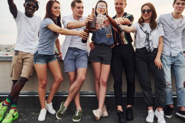 Alkolle birlikte çatının kenarında duruyor. Gündelik giysiler içinde bir grup genç gündüz vakti birlikte bir parti veriyor..