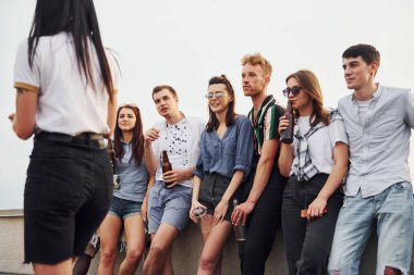 Ellerinde alkol ve telefonlarla dikiliyorsun. Gündelik giysiler içinde bir grup genç gündüz vakti çatıda parti veriyor..