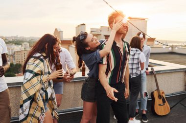 Oyun oynuyorum. Adamın gözleri ellerle kaplıydı. Gündelik giysiler içinde bir grup genç gündüz vakti çatıda parti veriyor..