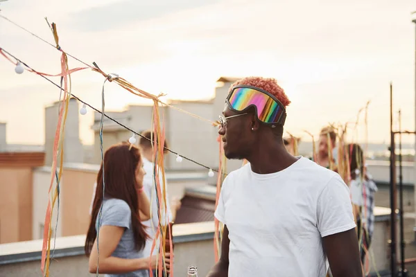 Kamera için poz vermek. Gündelik giysiler içinde bir grup genç gündüz vakti çatıda parti veriyor..