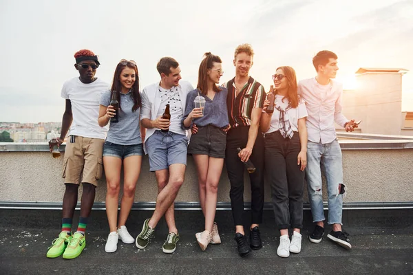 Alkolle birlikte çatının kenarında duruyor. Gündelik giysiler içinde bir grup genç gündüz vakti birlikte bir parti veriyor..