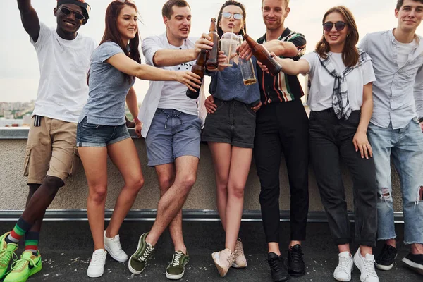 Alkolle birlikte çatının kenarında duruyor. Gündelik giysiler içinde bir grup genç gündüz vakti birlikte bir parti veriyor..