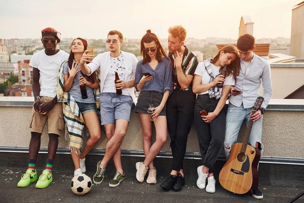 Ellerinde alkol ve telefonlarla dikiliyorsun. Gündelik giysiler içinde bir grup genç gündüz vakti çatıda parti veriyor..